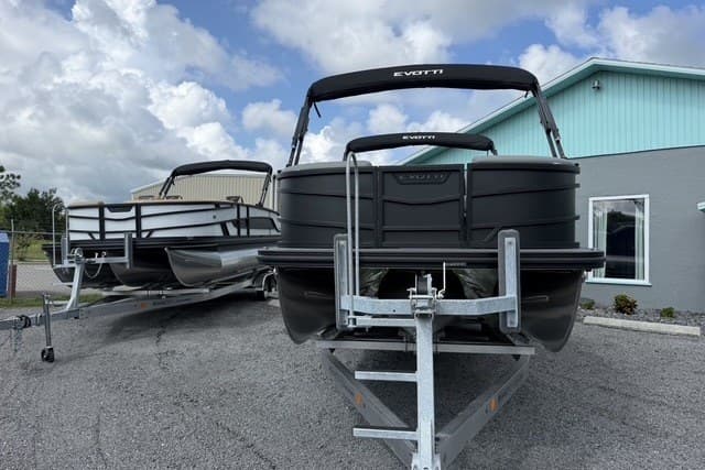 2027 Evotti 523CS pontoon boats on trailers, parked outside a building under a cloudy sky.