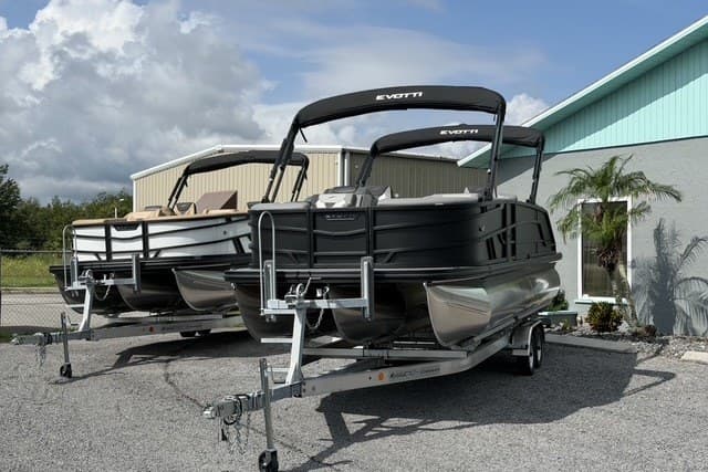 Two 2027 Evotti 523CS pontoon boats on trailers, parked outdoors near a building.